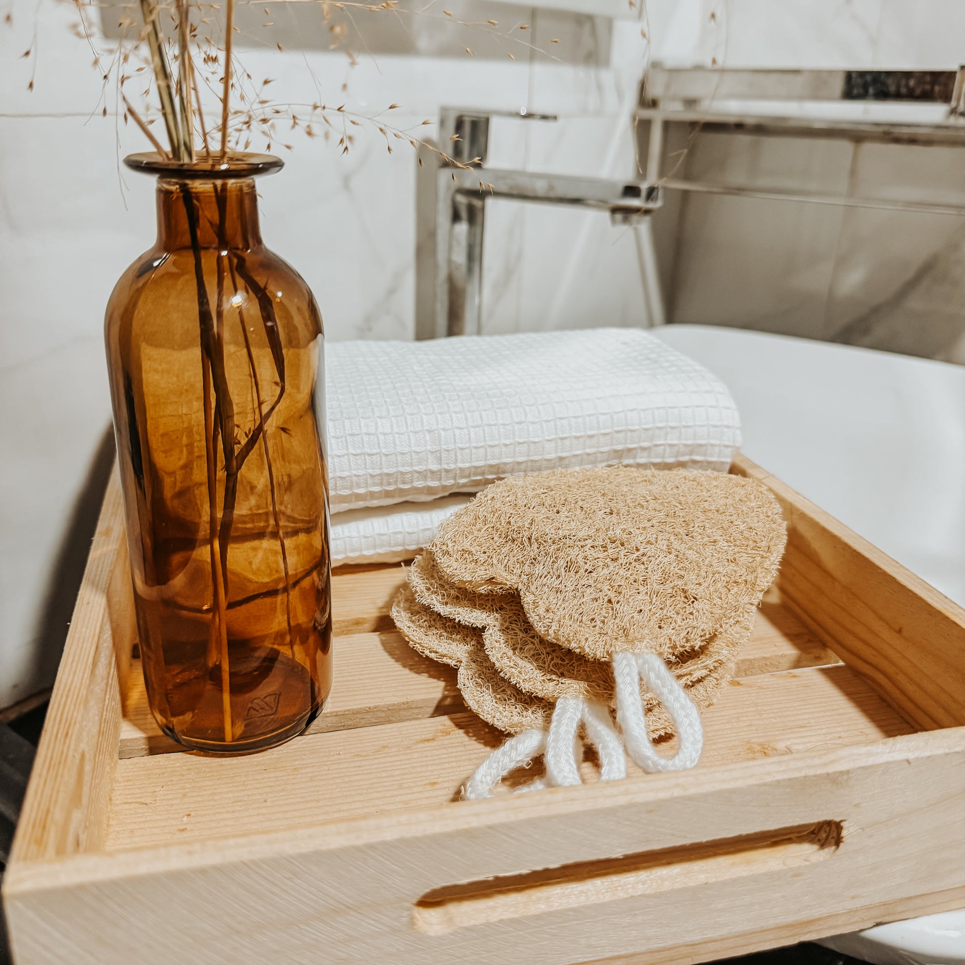 Jaivik Store organic heart-shaped loofah sponge displayed on a wooden tray with a towel and dry flowers, showcasing natural bath care products