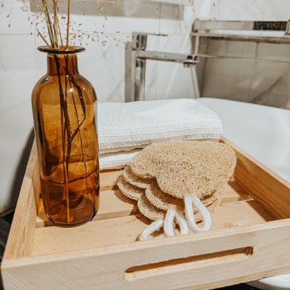 Jaivik Store organic heart-shaped loofah sponge displayed on a wooden tray with a towel and dry flowers, showcasing natural bath care products